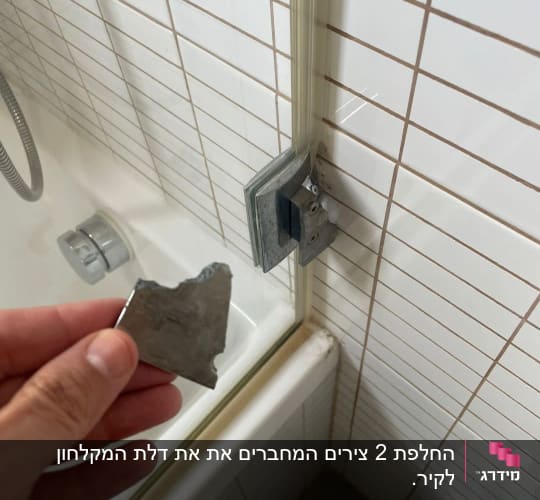 יד מחזיקה חלק מתכת שבור ליד דלת מקלחון